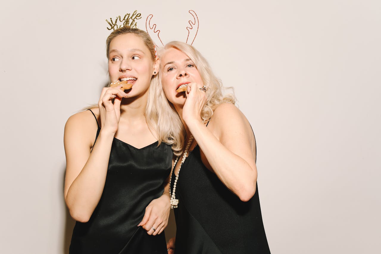 Two women enjoying holiday cookies, wearing festive attire with holiday headbands.